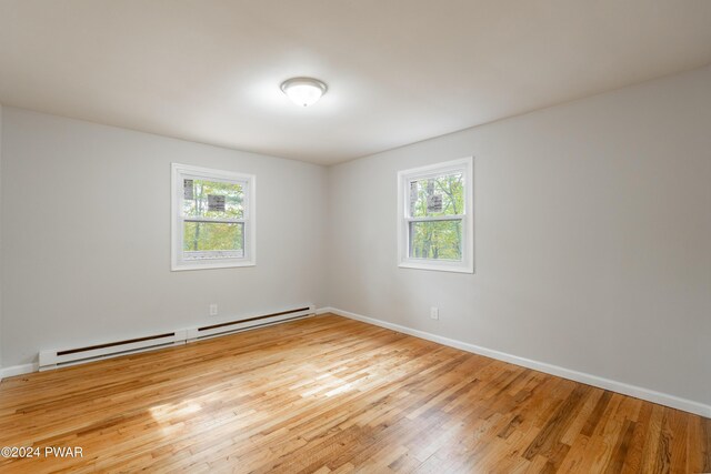 unfurnished room featuring plenty of natural light, light wood-type flooring, and a baseboard heating unit