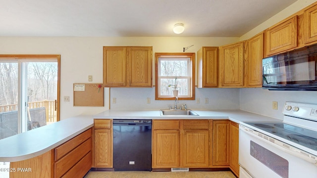 kitchen featuring visible vents, a peninsula, light countertops, black appliances, and a sink