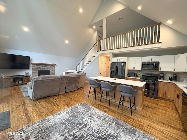 1006 Redlawn Ln, Lake Ariel, PA 18436 - kitchen with high vaulted ceiling, stainless steel appliances, a kitchen bar, light wood-type flooring, and a stone fireplace