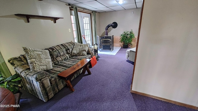 living area featuring a paneled ceiling, baseboards, a wood stove, and carpet