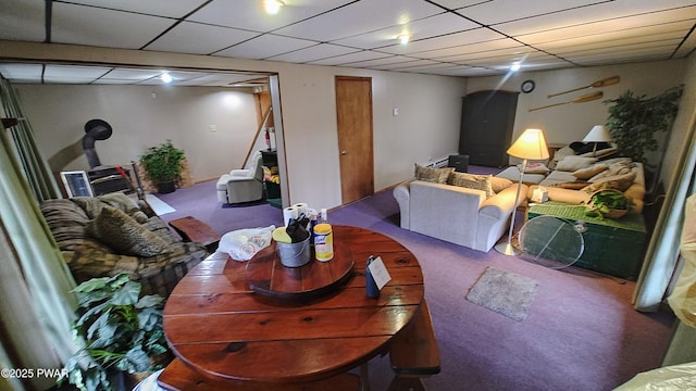 carpeted living area with a paneled ceiling and a wood stove