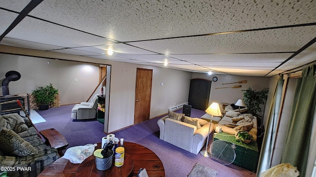 living room featuring a wood stove, a paneled ceiling, baseboards, and carpet floors