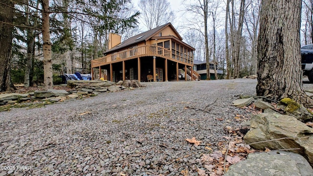 rear view of property featuring a wooden deck, a sunroom, a chimney, and stairway