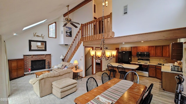 dining space featuring light wood-type flooring, high vaulted ceiling, ceiling fan with notable chandelier, a fireplace, and stairs