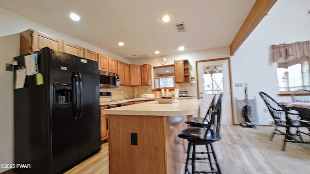 kitchen featuring light wood-type flooring, stainless steel microwave, a kitchen bar, and black fridge with ice dispenser