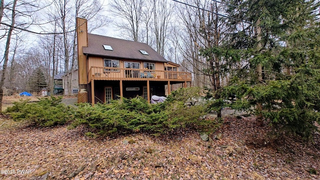 rear view of house featuring a wooden deck, roof with shingles, and a chimney