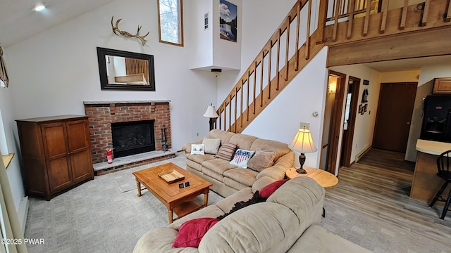 living room featuring stairway, a brick fireplace, light wood-type flooring, and a high ceiling