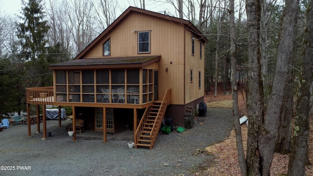 back of property with stairway, a shingled roof, a deck, and a sunroom