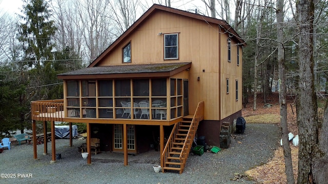 back of property with a wooden deck, stairs, roof with shingles, and a sunroom