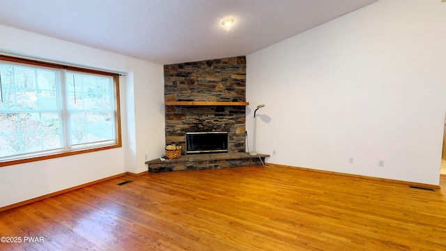 unfurnished living room featuring visible vents, lofted ceiling, wood finished floors, a stone fireplace, and baseboards