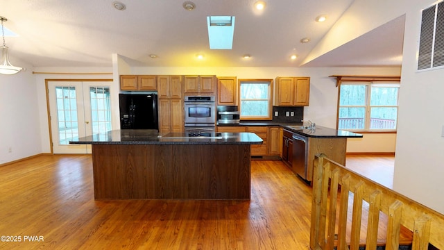 kitchen featuring lofted ceiling with skylight, a center island, light wood-type flooring, and stainless steel appliances