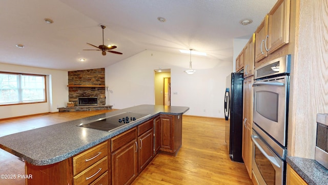 kitchen with dark countertops, light wood-type flooring, vaulted ceiling, a fireplace, and black appliances