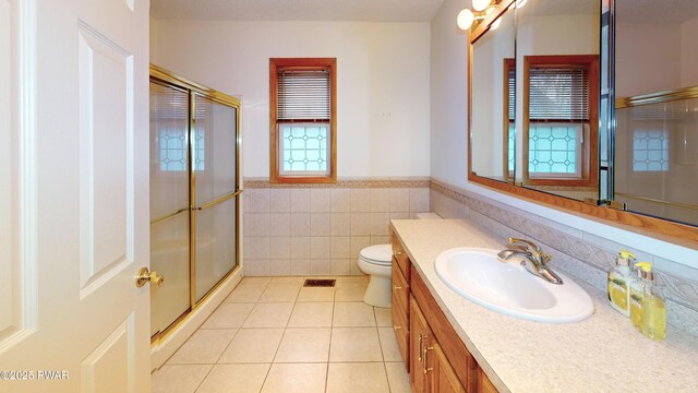 full bath featuring tile walls, wainscoting, a stall shower, tile patterned floors, and vanity