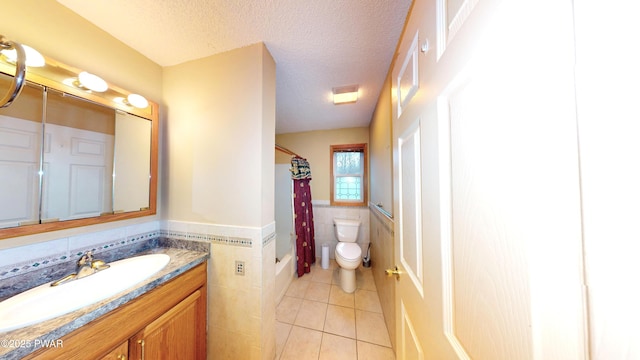 full bathroom featuring tile walls, a wainscoted wall, toilet, tile patterned floors, and a textured ceiling