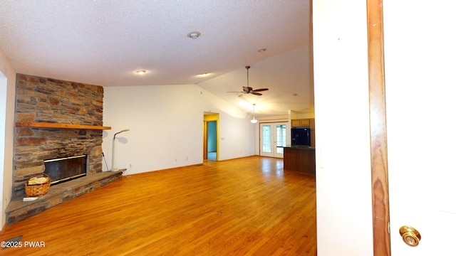 unfurnished living room with lofted ceiling, a fireplace, ceiling fan, light wood-style floors, and a textured ceiling