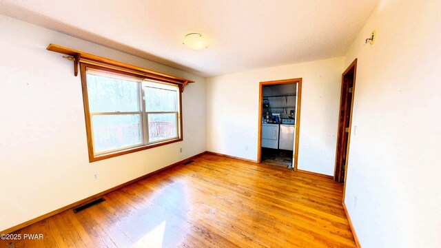 spare room featuring washer and dryer, visible vents, light wood-type flooring, and baseboards