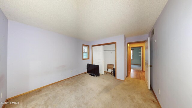 unfurnished bedroom featuring a closet, visible vents, light colored carpet, and a textured ceiling