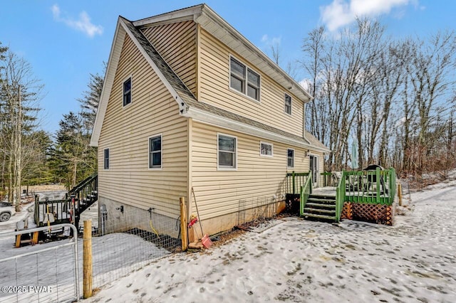 snow covered rear of property featuring a deck, stairs, and roof with shingles