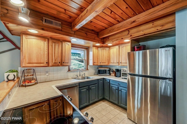 kitchen featuring appliances with stainless steel finishes, a sink, tile counters, light tile patterned floors, and decorative backsplash
