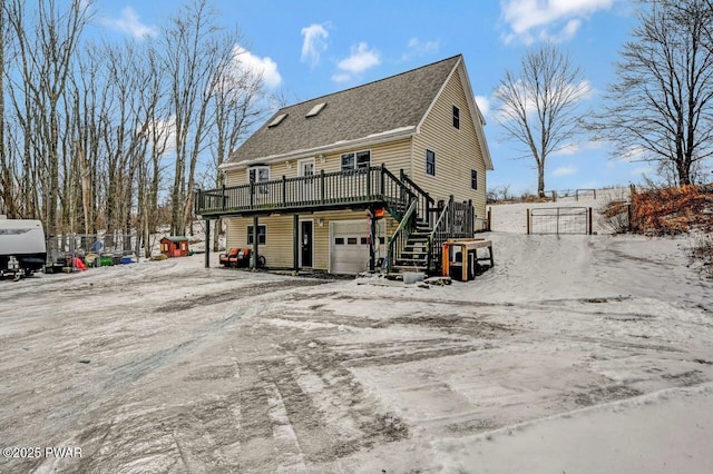 snow covered house with driveway, a garage, stairway, fence, and a deck