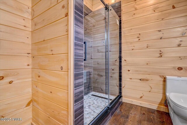 bathroom with wooden walls, wood-type flooring, a shower with shower door, and toilet