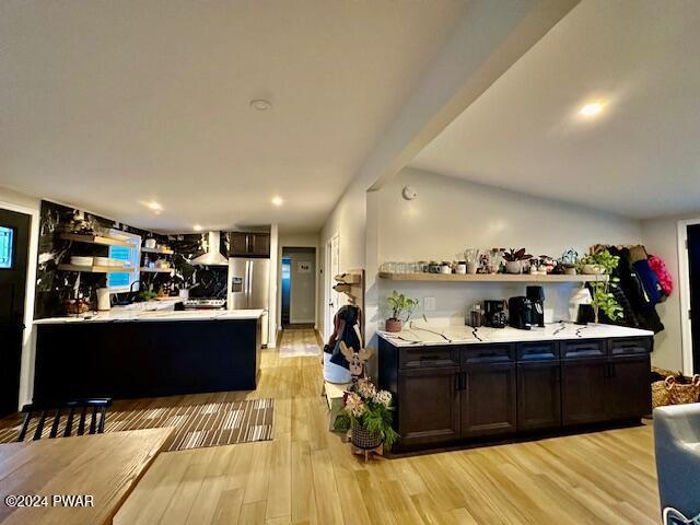 kitchen featuring dark brown cabinetry, stainless steel fridge with ice dispenser, range hood, and light hardwood / wood-style flooring