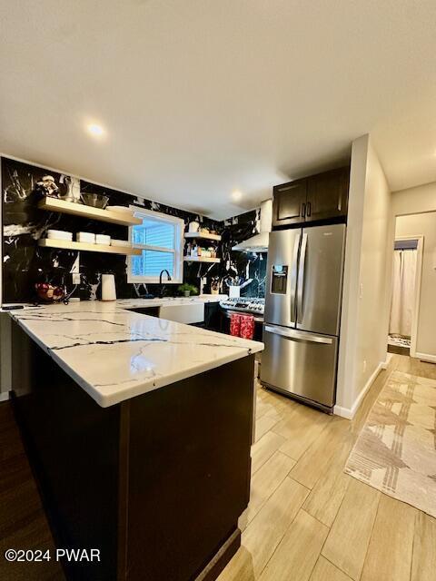 kitchen with kitchen peninsula, light stone counters, dark brown cabinetry, sink, and stainless steel fridge with ice dispenser