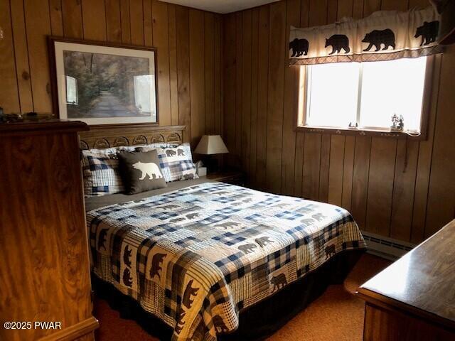 bedroom with baseboard heating, wood walls, and dark colored carpet