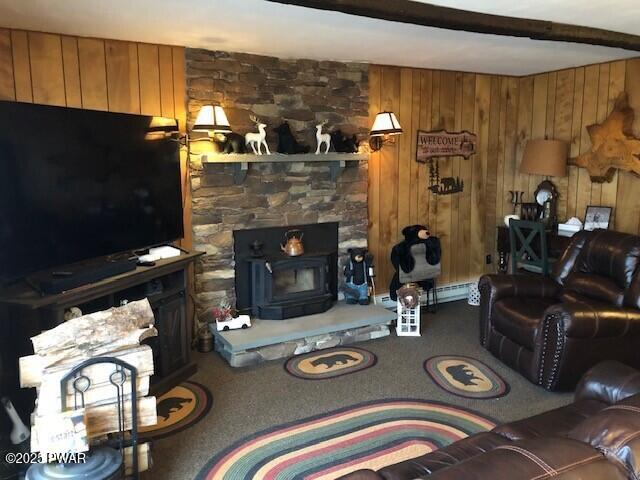 living room featuring beamed ceiling, wood walls, a wood stove, and carpet