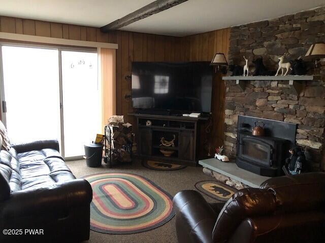 living room with beam ceiling, a wood stove, wooden walls, and light carpet