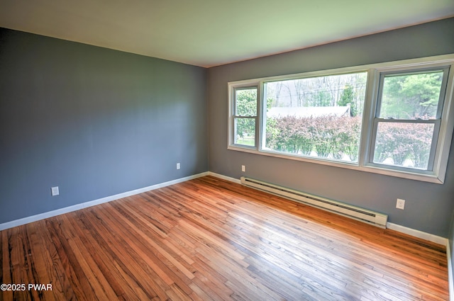 spare room featuring baseboards, a baseboard heating unit, and hardwood / wood-style flooring