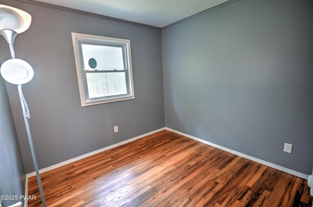 spare room with crown molding, baseboards, and wood finished floors