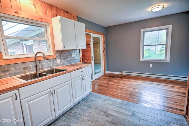 kitchen with backsplash, baseboard heating, white cabinetry, a sink, and butcher block countertops