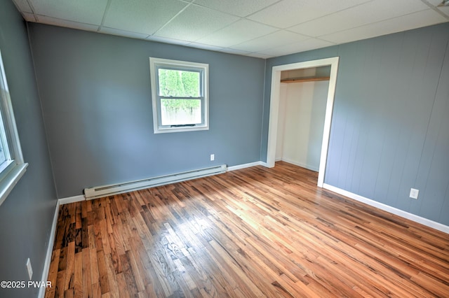 unfurnished bedroom with baseboards, a baseboard heating unit, a paneled ceiling, and hardwood / wood-style flooring