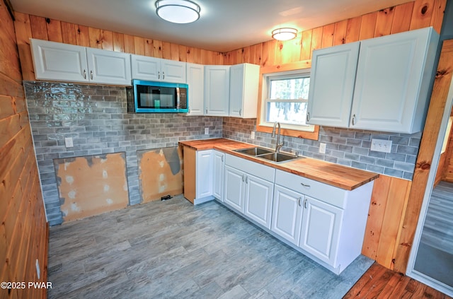 kitchen featuring tasteful backsplash, wood finished floors, a sink, white cabinets, and butcher block counters