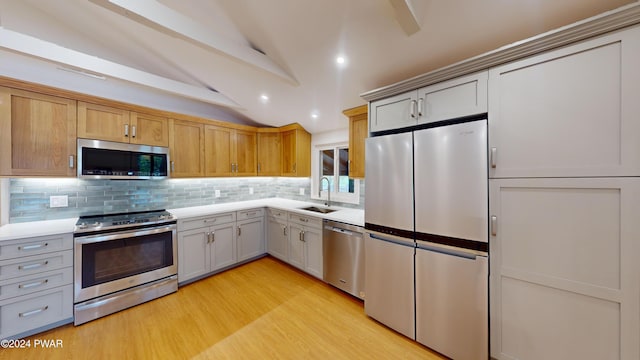 kitchen with sink, tasteful backsplash, vaulted ceiling, appliances with stainless steel finishes, and light wood-type flooring