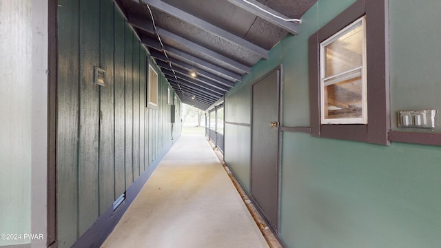 hallway with vaulted ceiling with beams, wooden walls, and concrete floors