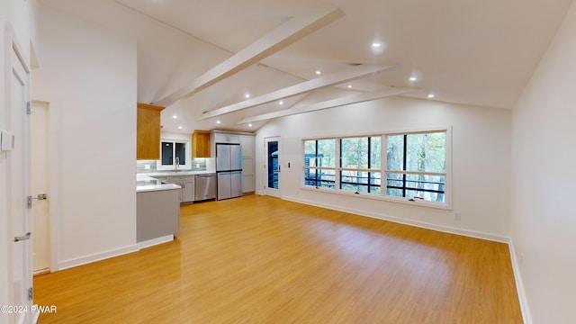 unfurnished living room with vaulted ceiling with beams, light hardwood / wood-style floors, and sink