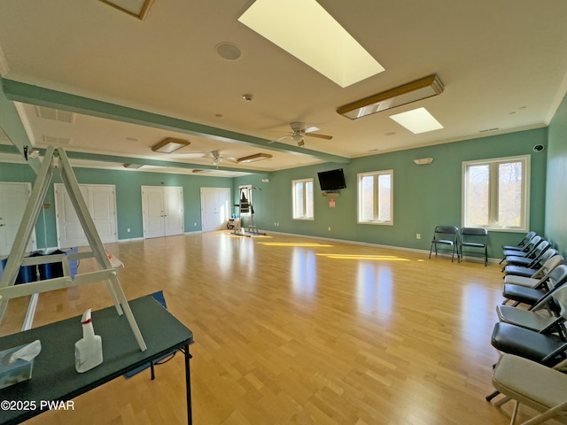 workout area featuring light wood-type flooring, a skylight, a healthy amount of sunlight, and ceiling fan