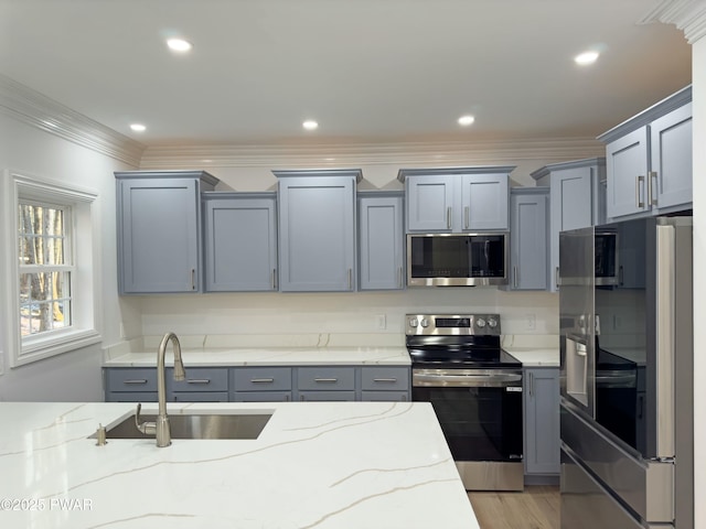 kitchen featuring sink, gray cabinetry, light stone counters, ornamental molding, and stainless steel appliances