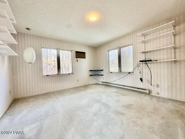 carpeted empty room with a textured ceiling, a baseboard radiator, and an AC wall unit