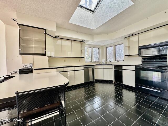 kitchen with a skylight, white cabinets, black appliances, and a textured ceiling