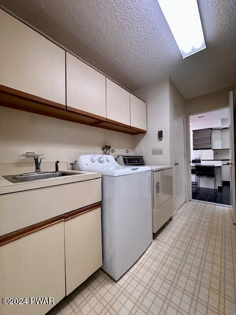 laundry area with cabinets, a textured ceiling, washer and dryer, and sink