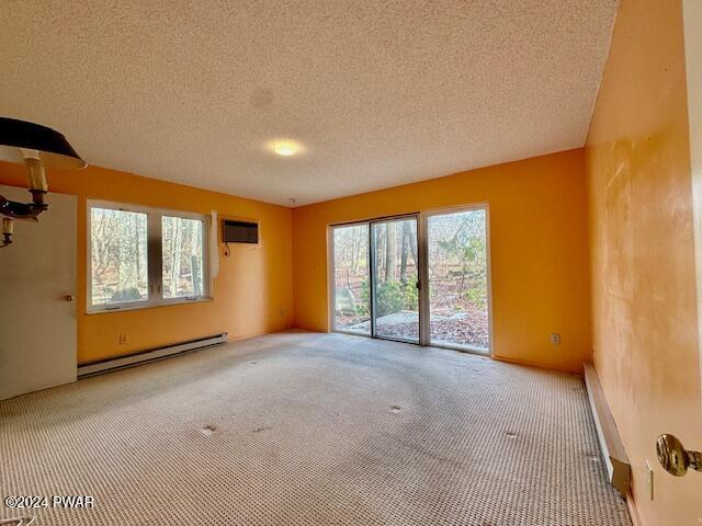 carpeted empty room with a textured ceiling, a baseboard radiator, and a wall mounted AC