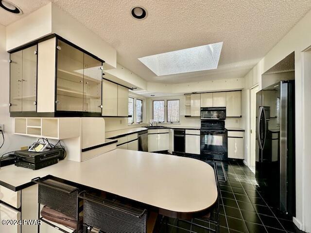 kitchen featuring a skylight, kitchen peninsula, black appliances, and a textured ceiling