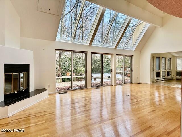 unfurnished living room featuring light hardwood / wood-style floors, a towering ceiling, and a skylight