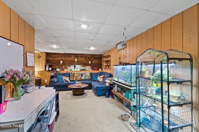 living room with carpet flooring, wood walls, and a drop ceiling