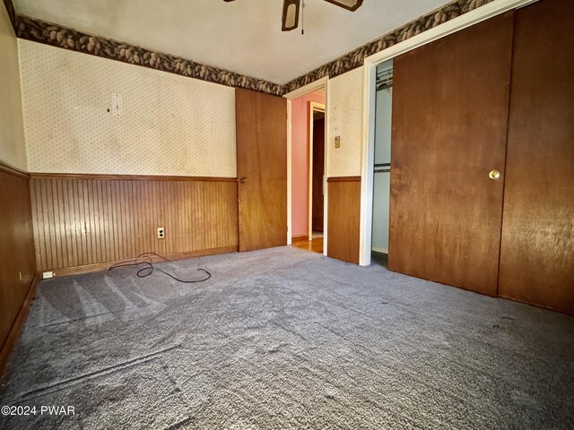 unfurnished bedroom featuring carpet, ceiling fan, and wooden walls