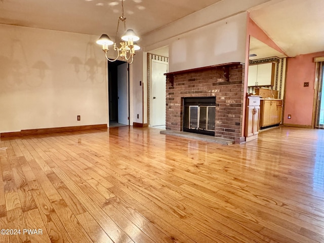 unfurnished living room with an inviting chandelier, light wood-type flooring, and a brick fireplace