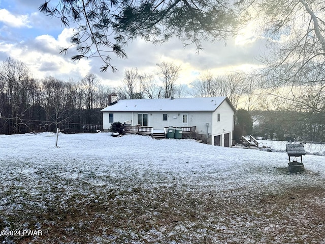 snow covered back of property featuring a garage and a wooden deck